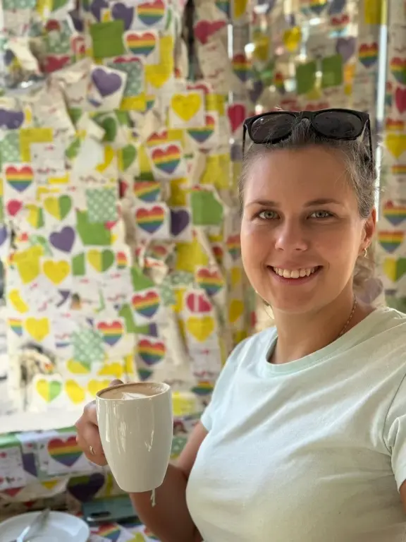 Veronika s kávou v kaviarni so stenou plnou farebných srdiečok